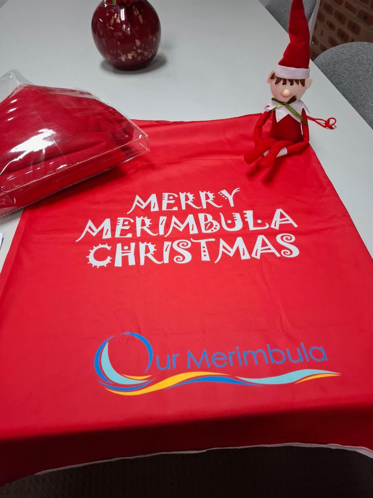 Red Merry Merimbula Christmas item with Our Merimbula logo and an elf